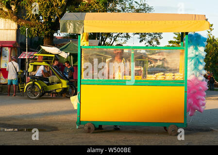 Cuartero, province de Capiz, Philippines : Young man selling popcorn et barbe colorée dans un petit panier poussoir jaune en fin d'après-midi Banque D'Images