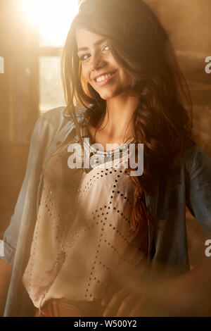 Side portrait of a smiling young woman standing fauve par la fenêtre Banque D'Images