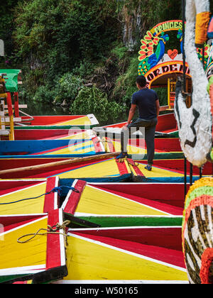 Xochimilco, Mexico City, 25 juin 2019 -homme debout sur le Emarcadero trajinera de Nativitas amarré parmi d'autres bateaux dans Xochimilco canal. Banque D'Images