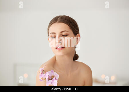 Belle jeune femme avec des fleurs d'orchidées dans spa salon Banque D'Images