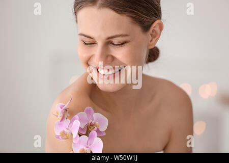 Belle jeune femme avec des fleurs d'orchidées dans spa salon Banque D'Images