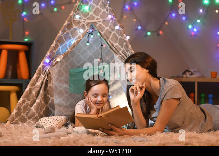 Mère et sa petite fille reading book in soir Banque D'Images