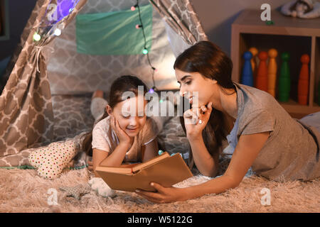 Mère et sa petite fille reading book in soir Banque D'Images