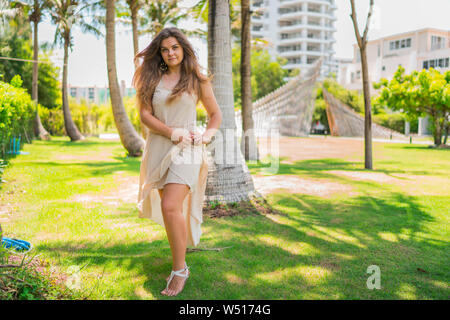 Attractive young woman in robe beige avec ses cheveux au vent debout sous les palmiers sur une journée ensoleillée en Thaïlande Banque D'Images