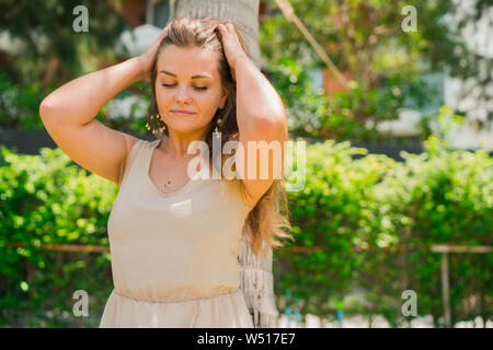 Close up portrait of attractive young woman standing under palm tree à la recherche vers le bas et de toucher ses cheveux avec les mains Banque D'Images