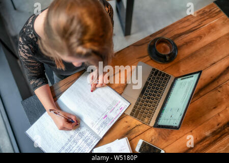 Girl sitting at table in cafe avec une tasse de chocolat chaud working on laptop et écrit dans l'ordinateur portable Banque D'Images
