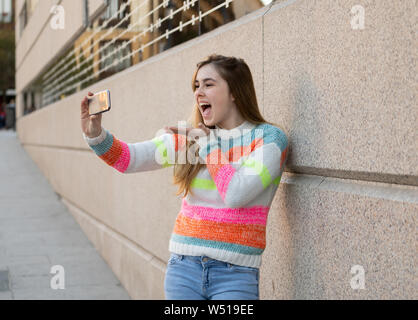 Heureux jolie fille adolescente à l'aide de smart mobile phone heureux soufflant un baiser et forme à des disciples des amis ou de la famille de l'enregistrement vidéo et de chatter. Vide Banque D'Images