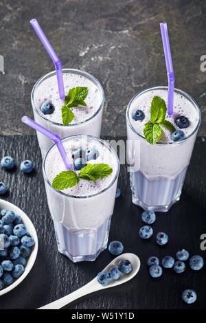 Smoothie aux bleuets mousse de lait de coco dans trois verres avec paille sur un plateau en ardoise noire sur une table en béton, vertical Vue de dessus Banque D'Images