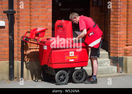 Un postier recueille mail pour la livraison à partir d'un poste électrique de livraison du courrier Royal ronde chariot ou panier main Banque D'Images