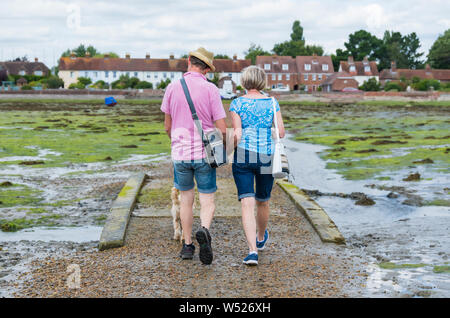 Un couple holding hands walking across Bosham Causeway à marée basse dans le port de Chichester, Bosham Village, West Sussex, Angleterre, Royaume-Uni. Banque D'Images