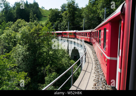 Saint Pierre, GR / Suisse - 24. Juillet, 2019 : red train à voie étroite de passage sur un pont de pierre sur un tronçon de voie sinueuse dans les Alpes suisses sur la Banque D'Images