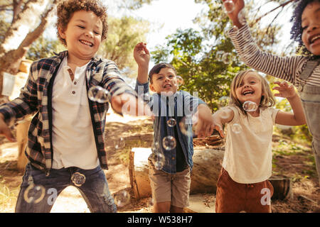 Groupe de quatre enfants s'amusant avec des bulles de savon dans la forêt. Les amis d'essayer d'attraper les bulles, à jouer ensemble. Banque D'Images