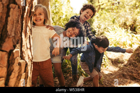 Cute smiling kids, à l'arrière l'arbre dans le parc. Groupe d'enfants profitant joue à cache-cache dans une forêt. Banque D'Images
