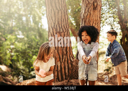 L'éclatement des filles les ballons d'eau avec les mains dans un parc. Groupe d'enfants s'amusant dans la forêt. Banque D'Images