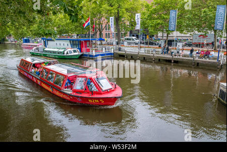 Les touristes de prendre une excursion en bateau sur le canal de nombreux canaux autour de la ville néerlandaise d'Amsterdam. Banque D'Images