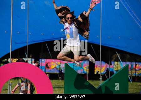 Malmesbury, Wiltshire. 26 juillet 2019. Un festival goer saute d'un signe comme Womad le festival se poursuit ce matin avec des températures d'hier après la chaleur record à l'échelle du pays. - Womad World of Music, Arts and Dance festival qui a eu lieu dans le magnifique parc du Charlton Park. Credit : Casper Farrell/Alamy News Banque D'Images