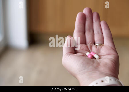 Une femelle adulte d'âge moyen qui tient deux, deux-pièces, de gélatine ou d'encapsulation gel couleur gélatine gélules de médicaments dans la paume de sa main. Banque D'Images