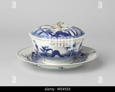 Bol à couvercle avec support avec des dames dans un paysage plat, bol de porcelaine avec couvercle, décor peint en bleu. Représentation continue d'une terrasse clôturée avec deux dames chinoises (les lignes trop longues) représenté deux fois, et quatre palmiers et deux de bananiers. Trois branches de pêchers à l'arrière. La face inférieure marquée avec la marque à six caractères de l'Empereur Kangxi dans un double cercle. Bleu Blanc., anonyme, la Chine, l'c. 1700 - c. 1724, Qing Dynasty, Kangxi (1644-1912) / (1662-1722) Période / Yongzheng-période (1723-1735), Porcelaine, glaçure (matériel), le cobalt (minéral), biscuit (porcelaine, matériel), de l'argent Banque D'Images