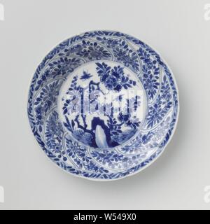 Saucer avec panneaux torsadés et sprays de fleurs, plat en porcelaine avec paroi ronde modélisé dans dix boîtes torsadée, peint en bleu sous glaçure. Sur la télévision un rocher avec une branche de fleurs, plantes et deux papillons, une fleur branche sur le mur dans chaque compartiment, la frontière avec une fleur de vigne, à l'arrière aussi une fleur branche dans chaque compartiment. Inscrite sur le fond avec le caractère chinois "Fú' dans un double cercle. Une puce dans le bord. Bleu Blanc., Fú', anonyme, la Chine, l'c. 1680 - c. 1720, Qing Dynasty, Kangxi (1644-1912) / (1662-1722) période, Porcelaine, glaçure (matériel), le cobalt (minéral), la vitrification Banque D'Images