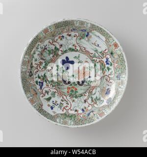 Avec le plat de soucoupe (mythologique) animaux, le paysage et les sprays de fleurs, plat en porcelaine avec mur de ronde, peinte en bleu sous glaçure et sur l'émail bleu, rouge, vert, jaune, aubergine, noir et or. Sur l'étagère un médaillon avec deux oiseaux et les sprays de fleurs, autour du médaillon quatre compartiments avec un feng huang, un paysage avec un chiffre dans un bateau, un qilin et symboles chanceux, dans entre quatre petits compartiments avec les plantes à fleurs, entre les fleurs et papillons des boîtes aérosols contre une masse verte mouchetée noire, la frontière avec fleur stylisée de vignes dans un cartouche entrecoupées Banque D'Images