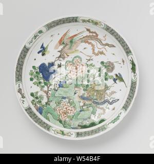 Plat de soucoupe avec des roches, des fleurs et feng huangs, avec soucoupe en porcelaine ronde, l'épandage, mur peint en bleu sous glaçure et au-dessus de la glaçure bleu, rouge, vert, jaune, Aubergine et noir. Sur les pierres plates avec la floraison de la pivoine et de deux branches, d'autres feng huangs les oiseaux et les insectes, la frontière avec motif géométrique alternant avec des symboles chanceux (castagnettes, sceptre, livre morte, musique Pierre, feuille d'artemisia) en cartouches. Le bas avec trois sprays de fleurs. Marqués d'un sceau marque dans un double cercle. Quatre jetons dans l'edge. Famille verte., anonyme, la Chine, l'c. 1700 - c. 1724, dynastie Qing- Banque D'Images