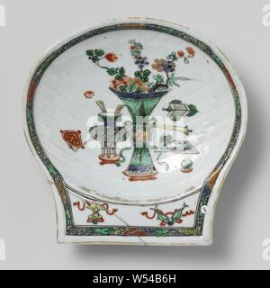 En forme de coquille de pétoncle bol avec antiquités, Bol en porcelaine en forme de coquillage, côtelées, mur peint sur l'émail en bleu, rouge, vert, jaune, aubergine, noir et or. Sur le fond d'antiquité (vase à fleurs, un sceptre ruyi, encens, etc.), sur la poignée de la chance deux symboles (parasol, poissons), en bordure des vignes de lotus stylisé sur un fond vert moucheté noir. Poignée arrière non vitrés, restaurée avec 5 agrafes. Famille verte., anonyme, la Chine, l'c. 1700 - c. 1724, Qing Dynasty, Kangxi (1644-1912) / (1662-1722) Période / Yongzheng-période (1723-1735), Porcelaine, glaçure (matériel), le cobalt (minéral), de l'or Banque D'Images