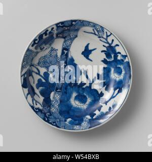 Soucoupe-plat avec un spray de fleurs, d'oiseaux et de fruits avec panneaux festonnés de couches et les sprays, modèle plat en porcelaine avec un mur de ronde et une épaisse, s'est bord, peint en bleu sous glaçure. Un peu plus de la moitié de l'avant une fleur branche avec deux grandes fleurs et un oiseau en vol, de plus, une bande décorative sur le plateau avec des feuilles de vigne et le travail de serviette. De l'autre côté de cette ceinture cartouches avec une fleur à la normande, la direction générale de la direction générale des pêches de vignes, feuille ou une serviette. La frontière avec feuilles détachées. Six médaillons à la chance des symboles sur le mur extérieur. Une puce dans le bord. Arita, bleu et blanc Banque D'Images