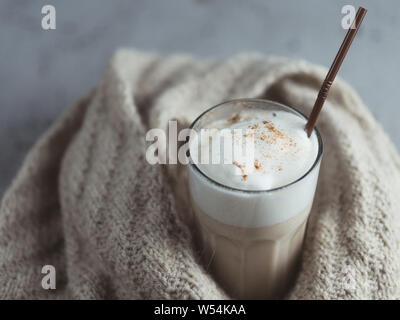 Un verre de café latte d'automne sur un tableau gris enveloppé dans une écharpe en tricot Banque D'Images