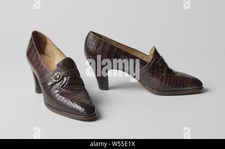 Pompe constituée d'un cuir de crocodile marron avec boucle couleur argent, à gauche de la pompe en cuir de crocodile marron avec boucle couleur argent. Modèle : The Deep-cut sur l'avant-pied est cousue en une langue et se termine à l'instep et dentelées sur le cou-de-pied. La langue est recouverte des deux côtés par des panneaux latéraux, qui sont décorées à l'extrémité d'une bordure en cuir marron. Ceux-ci sont reliés par une courroie d'une largeur de 1 cm qui se ferme sur l'extérieur de la couverture avec une boucle de couleur métallique. (7) cm de haut talon recouvert de cuir de crocodile. L'avant-pied est doublé de coton de couleur naturelle, le reste de la chaussure de cuir Banque D'Images