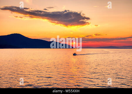 Voile sur la mer au coucher du soleil dans l'arrière-plan de montagnes et rayons de soleil, exécuté à partir de la ville à l'île de Thassos Keramoti en Grèce Banque D'Images