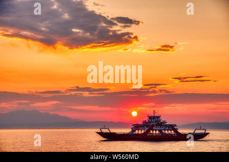 Ferry vers la mer au coucher du soleil dans l'arrière-plan de montagnes et rayons de soleil, exécuté à partir de la ville à l'île de Thassos Keramoti en Grèce Banque D'Images