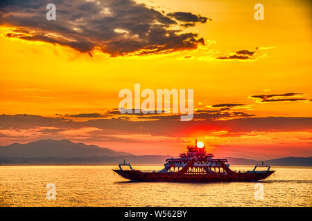 Ferry vers la mer au coucher du soleil dans l'arrière-plan de montagnes et rayons de soleil, exécuté à partir de la ville à l'île de Thassos Keramoti en Grèce Banque D'Images