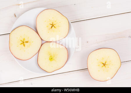 Groupe de l'un deux trois tranches de pommes Red Delicious, fraîches sur une petite plaque en céramique blanche sur flatlay bois blanc Banque D'Images