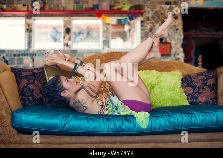 Hispanic woman relaxing at home dans un esprit créatif yoga pose sur son canapé. Banque D'Images