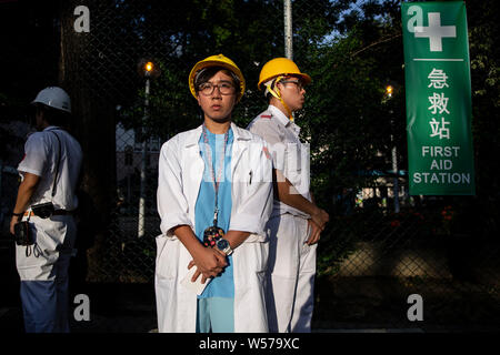 Les participants portent leur uniforme du personnel médical avec des casques pendant la manifestation.Des centaines de travailleurs médicaux y compris les médecins et les infirmières ont pris part à un rassemblement à l'Hôpital Queen Elizabeth de Hong Kong, afin de protester contre le projet de loi sur l'extradition et de condamner la violence par les gangs d'hommes à Yuen Long le 21 juillet. Banque D'Images