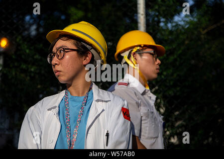 Les participants portent leur uniforme du personnel médical avec des casques pendant la manifestation.Des centaines de travailleurs médicaux y compris les médecins et les infirmières ont pris part à un rassemblement à l'Hôpital Queen Elizabeth de Hong Kong, afin de protester contre le projet de loi sur l'extradition et de condamner la violence par les gangs d'hommes à Yuen Long le 21 juillet. Banque D'Images