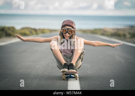 Jeune garçon blond joue aviator assis en tailleur sur planche avec les bras tendus pour voler smiling enfant imite plane flying sur piste de l'aéroport. Banque D'Images