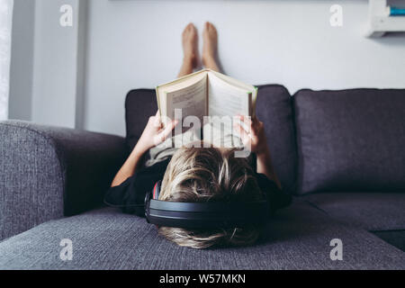 Garçon Blond nu lit livre et écoutant de la musique en position couchée. La leçon de lecture des élèves confortablement détendu, diligence enfant lit une histoire jeune homme p Banque D'Images