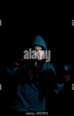 Portrait de jeune femme de l'exercice dans la salle de sport de boxe avec des gants rouge sur fond noir Banque D'Images