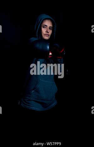 Portrait de jeune femme de l'exercice dans la salle de sport de boxe avec des gants rouge sur fond noir Banque D'Images