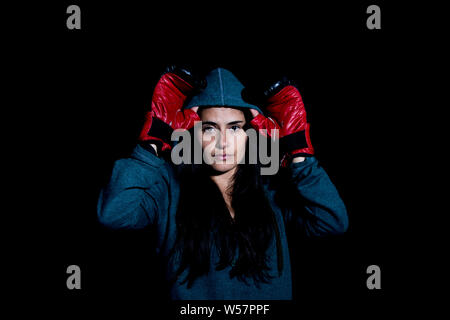 Portrait de jeune femme de l'exercice dans la salle de sport de boxe avec des gants rouge sur fond noir Banque D'Images