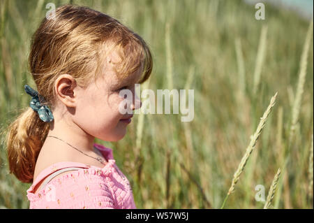 Vue latérale de la petite fille blonde adorable sourire timide avec standing in field sur Grotta île sur arrière-plan flou Banque D'Images