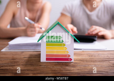 Close-up of a House montrant le taux d'efficacité énergétique en face de Couple Using Calculator Banque D'Images