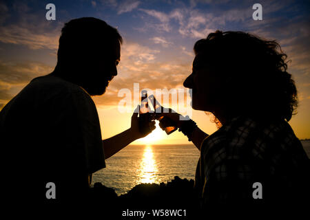 Couple heureux profiter de la bière sur la plage pendant le coucher du soleil. Leurs bouteilles de bière amateurs de trinquer à l'extérieur. Vacances romantiques. Deux aimant boire ensemble Banque D'Images