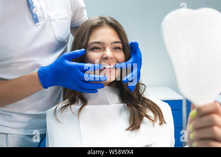 Belle jeune femme brune ayant l'examen préliminaire en cabinet dentaire dentiste blanchissant tout en montrant les résultats de patients satisfaits Banque D'Images