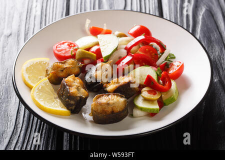 Tranches de poisson anguille frite avec une salade de légumes frais et de citron sur une plaque horizontale sur la table. Banque D'Images