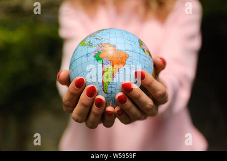 La Fille en rose avec un chandail rouge manucure est titulaire d'un petit globe géographique avec les noms en lettres cyrilliques ukrainiens sur elle. L'Amérique du Sud est visible Banque D'Images