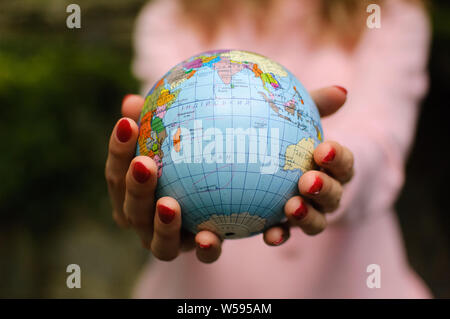 Les jeunes une adolescente en rose vêtements décontractés avec manucure rouge tenant un peu de monde avec des noms géographique en ukrainien les lettres cyrilliques sur elle en Banque D'Images