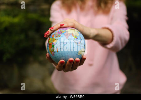 Les jeunes une adolescente en rose vêtements décontractés avec manucure rouge tenant un peu de monde avec des noms géographique en ukrainien les lettres cyrilliques sur elle en Banque D'Images