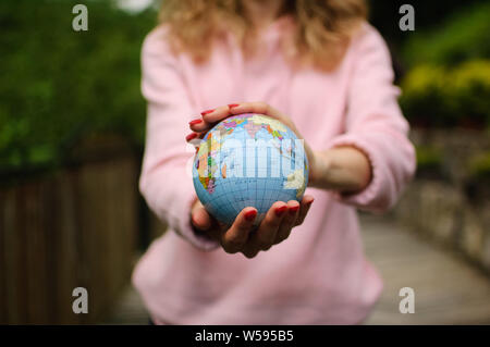 Les jeunes une adolescente en rose vêtements décontractés avec manucure rouge tenant un peu de monde avec des noms géographique en ukrainien les lettres cyrilliques sur elle en Banque D'Images